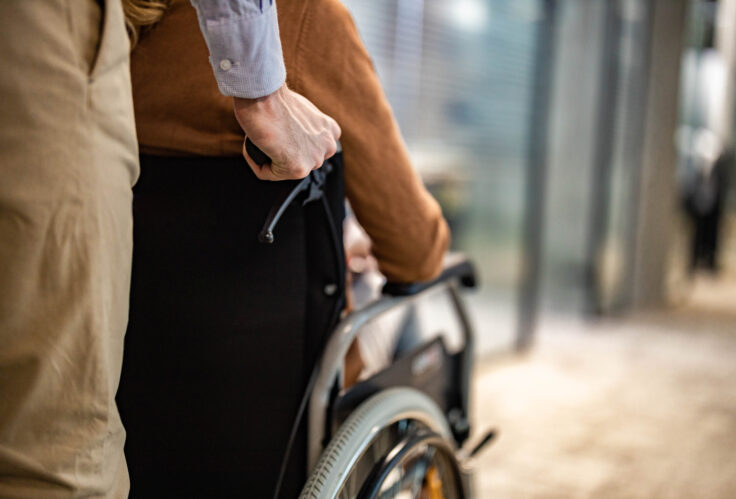 Close up of unrecognizable man pushing his friend in a wheelchair represents the need for disability protection