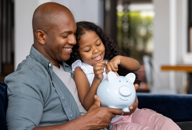 A father and daughter put money in a piggy bank to practice Financial literacy for families