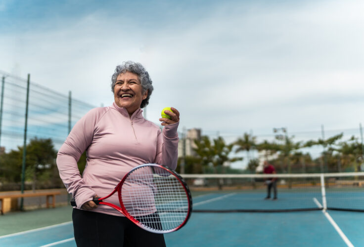 Senior woman playing tennis at sports court is someone who should work on coordinating Medicare & Retirement plans