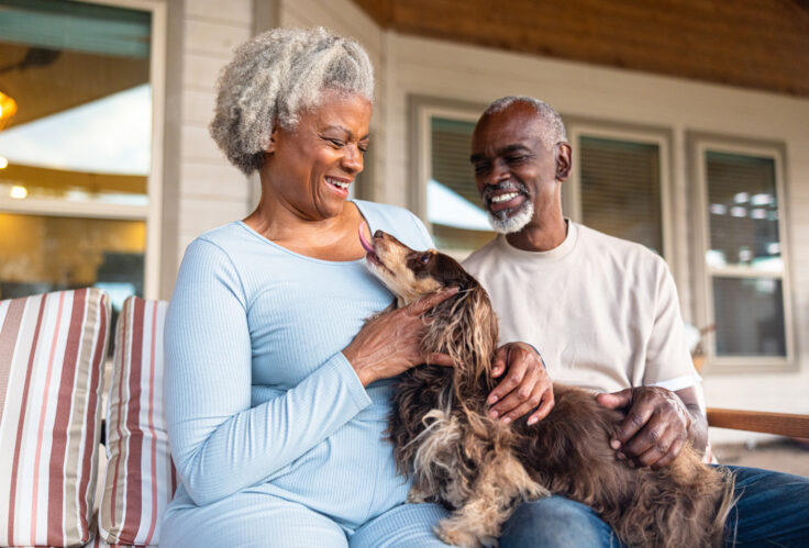 A Senior black couple at home cuddling with their longhaired dachshund dog enjoy retirement thanks to Risk Management for Retirement